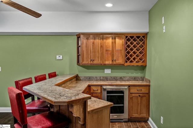 kitchen featuring dark wood-style floors, wine cooler, a breakfast bar area, a peninsula, and light countertops