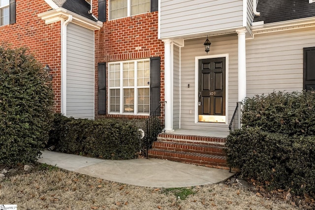 entrance to property with a shingled roof and brick siding