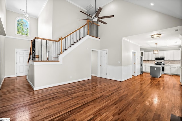 unfurnished living room featuring stairs, crown molding, a high ceiling, and wood finished floors