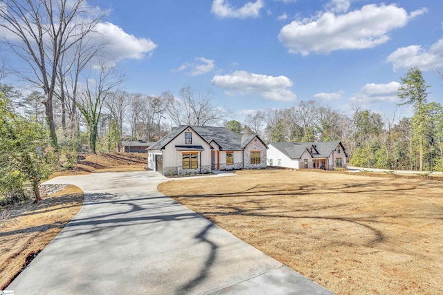 modern farmhouse featuring a front yard, stone siding, and concrete driveway