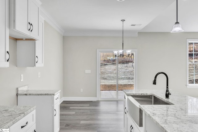 kitchen with wood finished floors, light stone counters, a sink, and ornamental molding