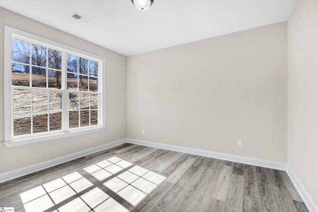 spare room with wood finished floors, visible vents, and baseboards