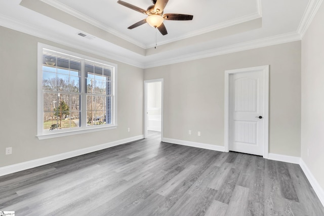 unfurnished room featuring a tray ceiling, wood finished floors, visible vents, and baseboards