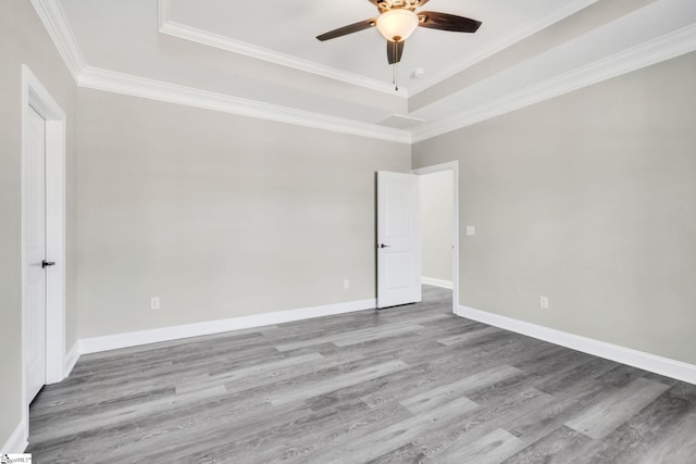 spare room featuring wood finished floors, a ceiling fan, baseboards, ornamental molding, and a tray ceiling