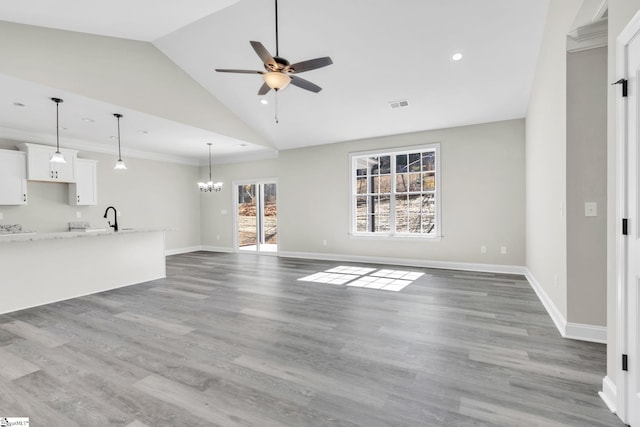 unfurnished living room featuring visible vents, vaulted ceiling, a sink, wood finished floors, and ceiling fan with notable chandelier