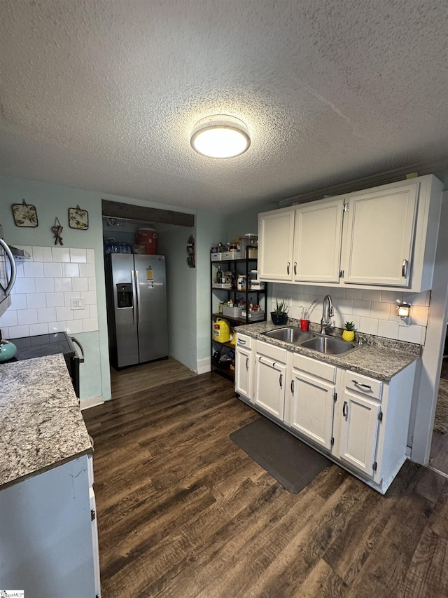 kitchen with dark wood finished floors, tasteful backsplash, white cabinetry, a sink, and stainless steel fridge