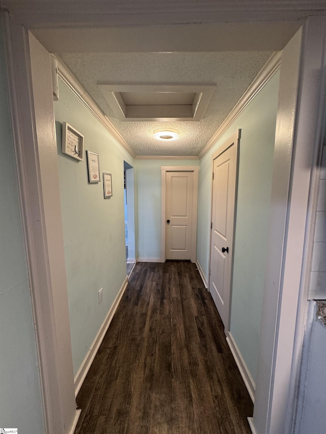 hallway with a textured ceiling, dark wood-style flooring, baseboards, ornamental molding, and attic access