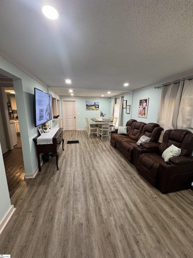 living room featuring a textured ceiling, baseboards, wood finished floors, and recessed lighting