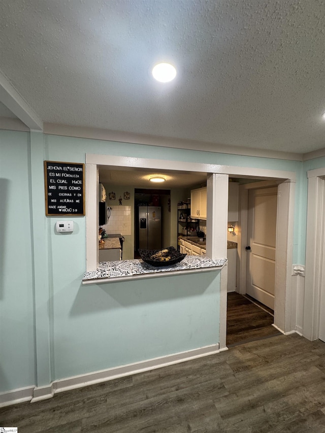 kitchen featuring dark wood finished floors, stainless steel refrigerator with ice dispenser, white cabinets, a textured ceiling, and baseboards