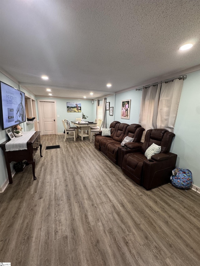 living room featuring a textured ceiling, baseboards, wood finished floors, and recessed lighting