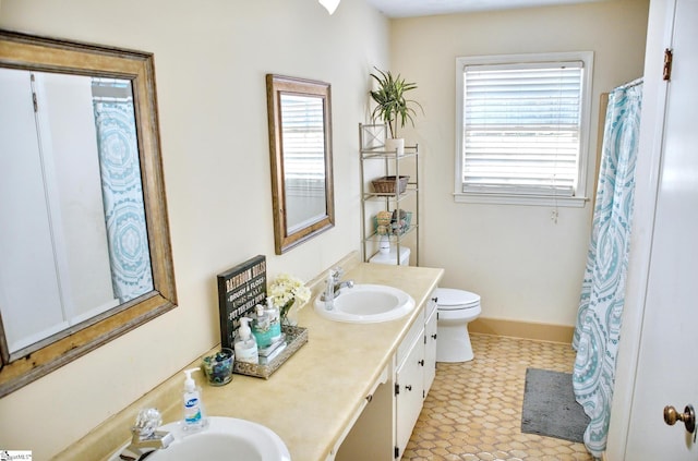 bathroom with toilet, double vanity, baseboards, and a sink