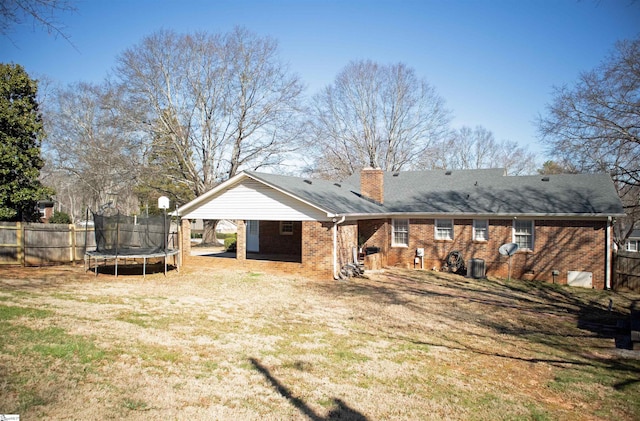 rear view of house featuring a trampoline, brick siding, and fence