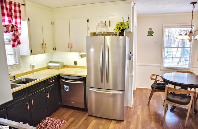 kitchen featuring crown molding, light countertops, appliances with stainless steel finishes, dark wood-type flooring, and wainscoting