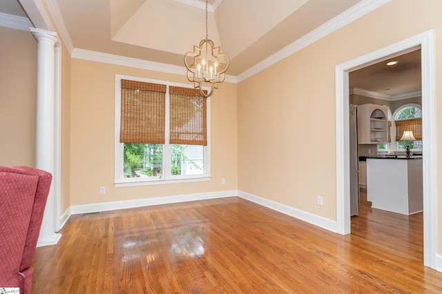 spare room featuring wood finished floors, baseboards, ornamental molding, ornate columns, and an inviting chandelier