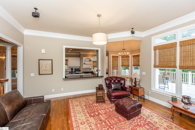 living room with crown molding, decorative columns, wood finished floors, a chandelier, and baseboards