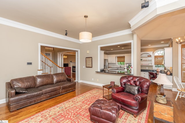 living room featuring baseboards, wood finished floors, an inviting chandelier, stairs, and crown molding