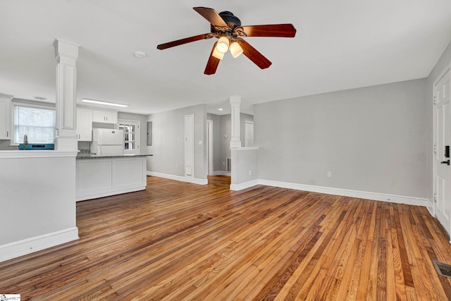 unfurnished living room featuring hardwood / wood-style flooring, decorative columns, and baseboards