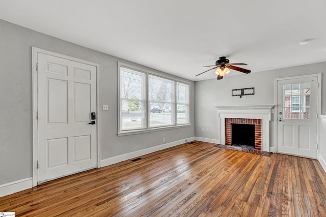 unfurnished living room with visible vents, baseboards, a ceiling fan, hardwood / wood-style floors, and a brick fireplace