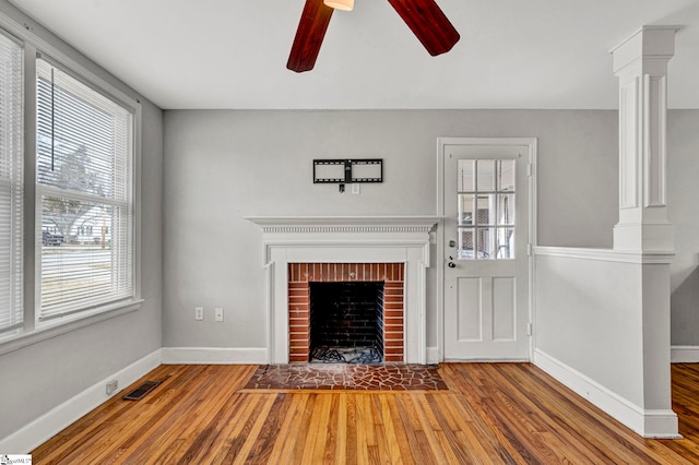 unfurnished living room featuring ornate columns, visible vents, a brick fireplace, wood finished floors, and baseboards