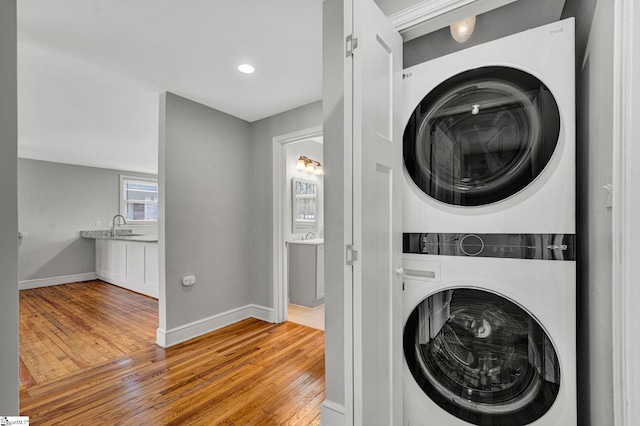 washroom featuring laundry area, baseboards, stacked washer and clothes dryer, hardwood / wood-style flooring, and a sink