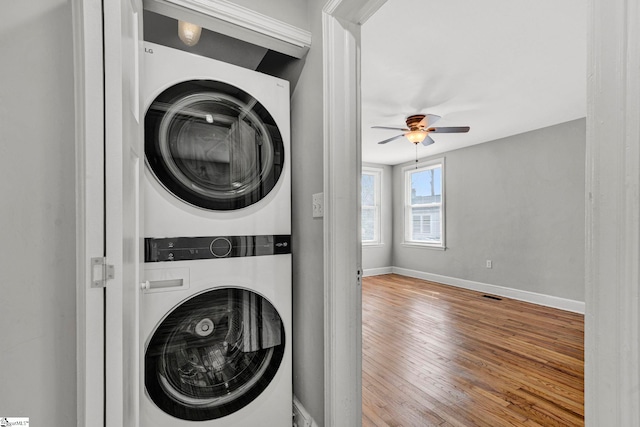 laundry area featuring laundry area, wood finished floors, a ceiling fan, baseboards, and stacked washing maching and dryer