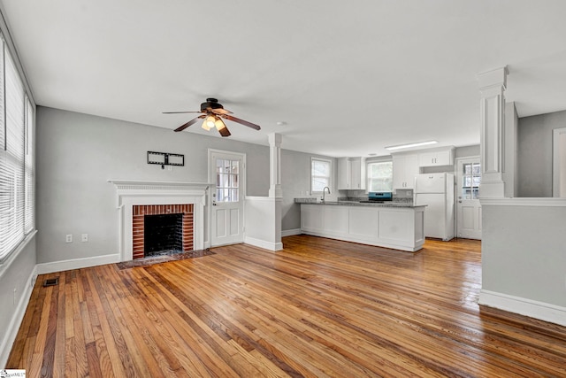 unfurnished living room with decorative columns, visible vents, baseboards, light wood-style flooring, and a brick fireplace