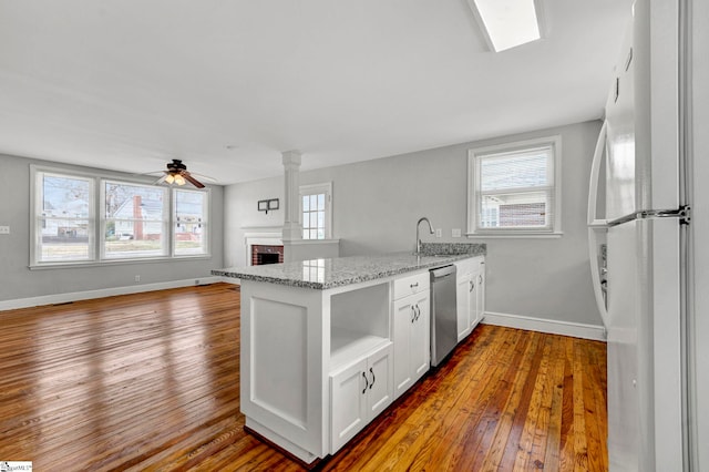 kitchen with wood-type flooring, freestanding refrigerator, a brick fireplace, open shelves, and stainless steel dishwasher