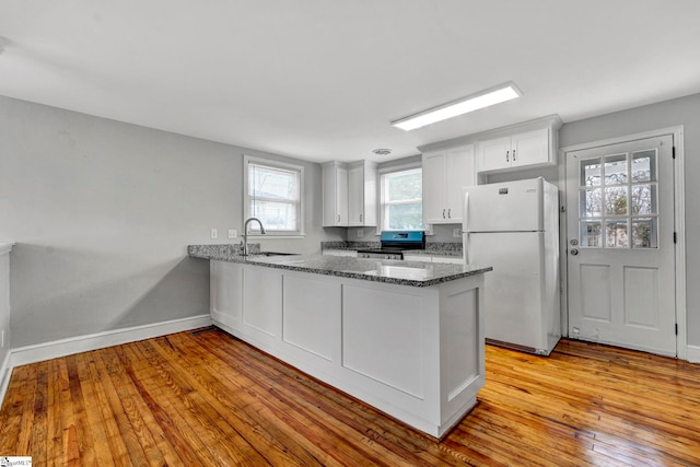 kitchen featuring electric stove, dark stone countertops, freestanding refrigerator, a peninsula, and a sink