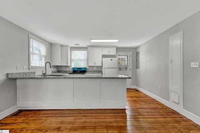 kitchen with a peninsula, a sink, stainless steel electric range, freestanding refrigerator, and dark stone countertops