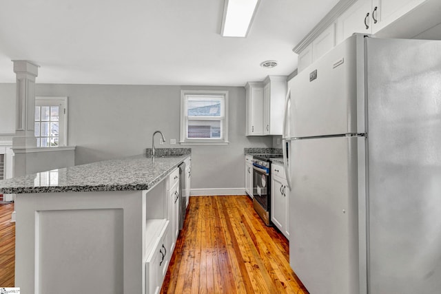 kitchen with stone countertops, freestanding refrigerator, stainless steel stove, light wood-style floors, and a sink