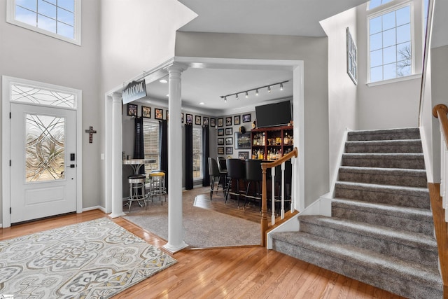 entrance foyer featuring a healthy amount of sunlight, stairway, wood finished floors, a bar, and ornate columns