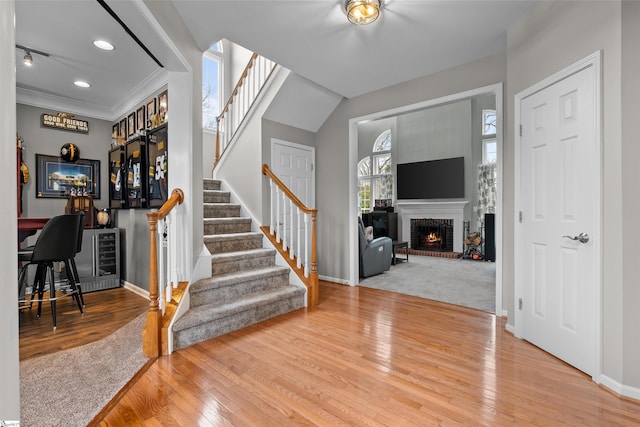 foyer with a fireplace, baseboards, stairway, wood-type flooring, and crown molding