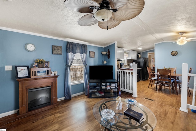 living area featuring light wood finished floors, baseboards, a ceiling fan, vaulted ceiling, and a textured ceiling