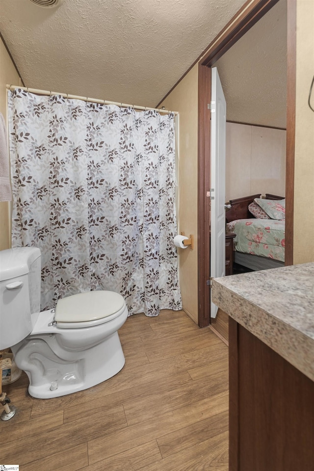 bathroom with a textured ceiling, curtained shower, toilet, wood finished floors, and vanity