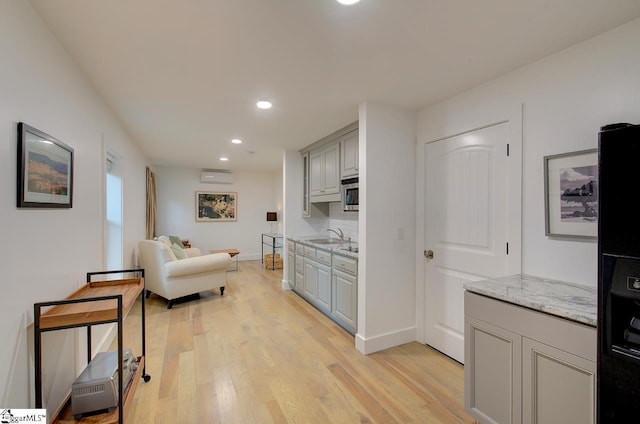 kitchen featuring stainless steel microwave, a sink, gray cabinetry, light wood-type flooring, and backsplash