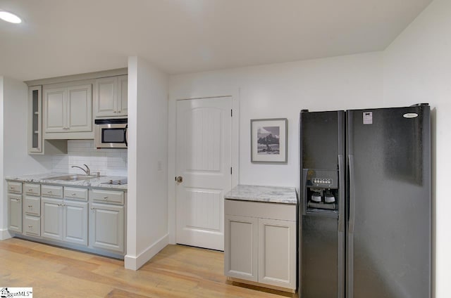 kitchen with gray cabinets, stainless steel microwave, black refrigerator with ice dispenser, backsplash, and light wood-style flooring