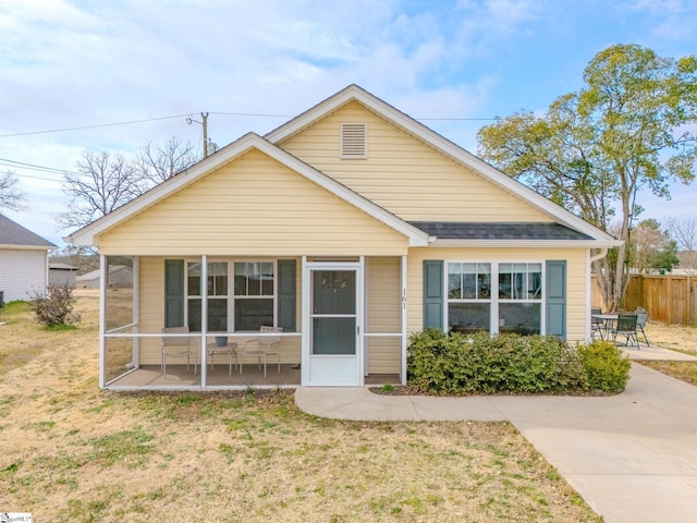 bungalow-style house featuring a sunroom, roof with shingles, fence, a patio area, and a front lawn