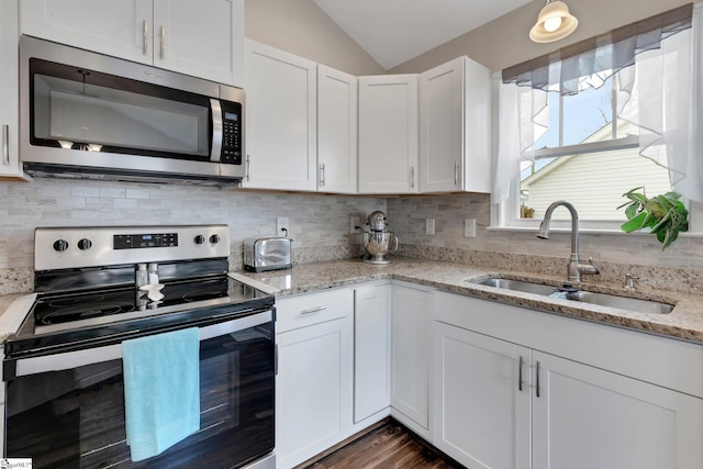 kitchen with tasteful backsplash, white cabinets, lofted ceiling, appliances with stainless steel finishes, and a sink