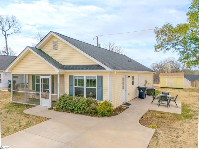 view of front of home with a shingled roof, a sunroom, an outbuilding, a storage unit, and a patio area