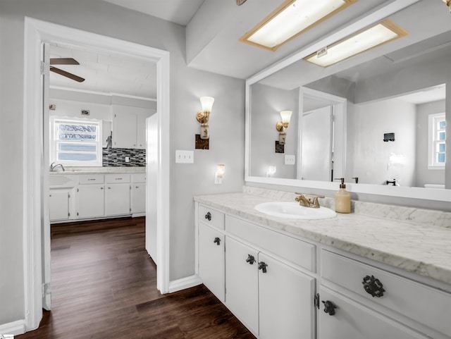 bathroom with wood finished floors, vanity, baseboards, a ceiling fan, and backsplash