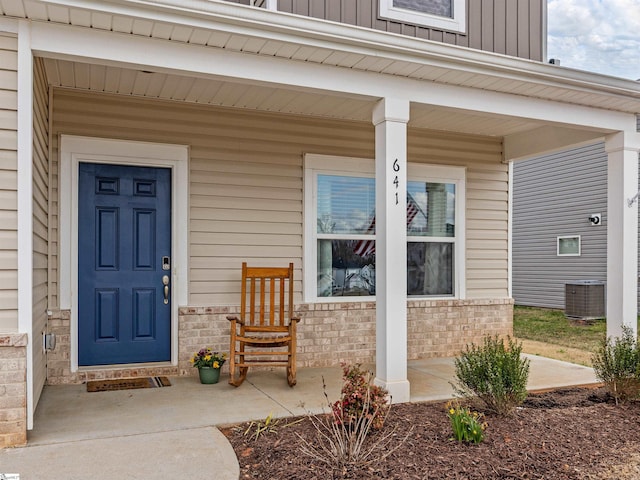 property entrance with board and batten siding, brick siding, a porch, and central air condition unit