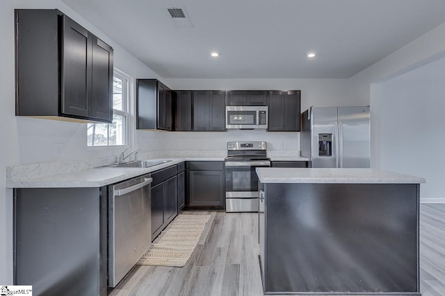 kitchen featuring light wood-style floors, a kitchen island, stainless steel appliances, and a sink