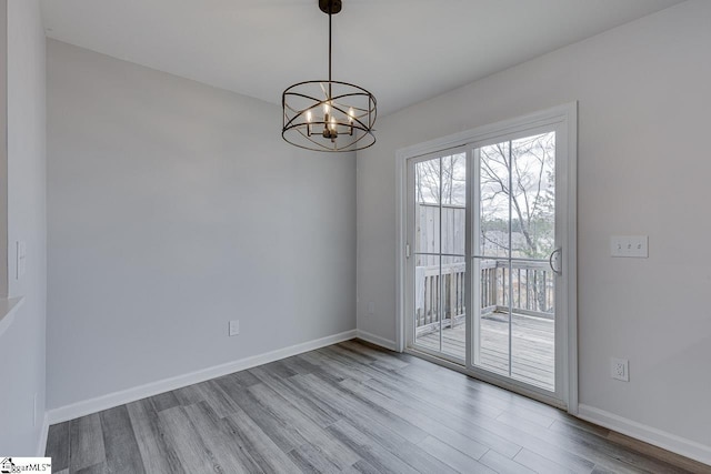 unfurnished room with a notable chandelier, baseboards, and wood finished floors