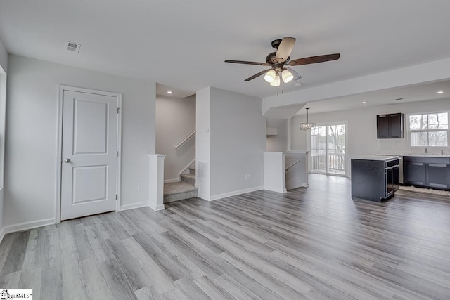 unfurnished living room with recessed lighting, ceiling fan with notable chandelier, wood finished floors, baseboards, and stairs