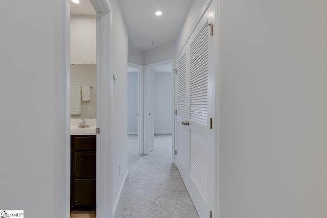 hall with recessed lighting, light colored carpet, a sink, visible vents, and baseboards