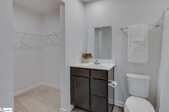 bathroom with a walk in closet, baseboards, vanity, and toilet