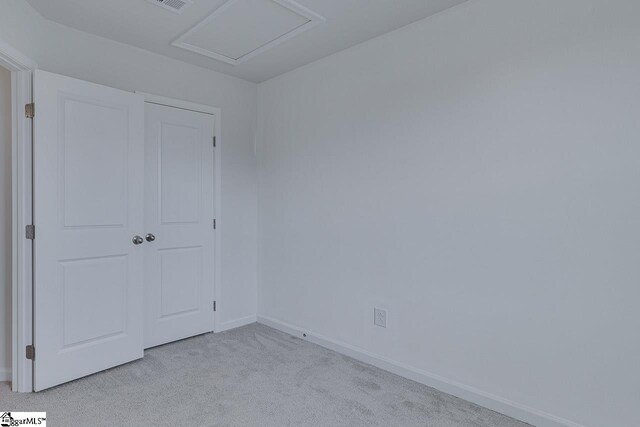 unfurnished bedroom featuring light carpet, attic access, and baseboards