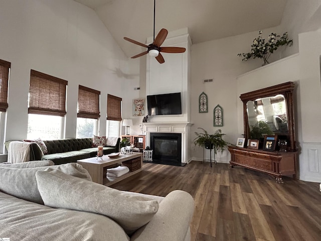 living area with visible vents, a ceiling fan, a glass covered fireplace, wood finished floors, and high vaulted ceiling