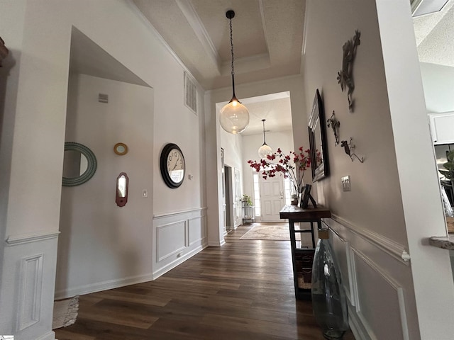 corridor with a wainscoted wall, a tray ceiling, dark wood finished floors, and a decorative wall