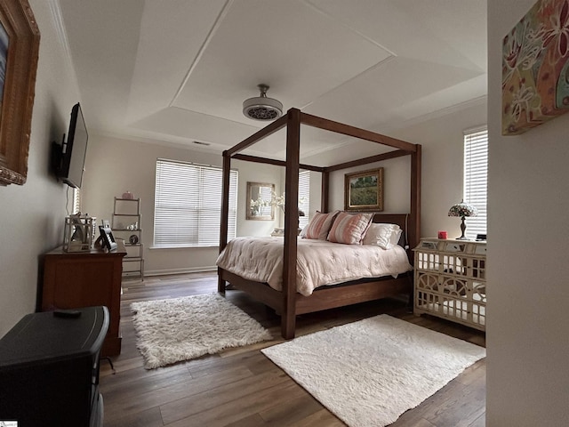 bedroom featuring a raised ceiling, ornamental molding, and wood finished floors